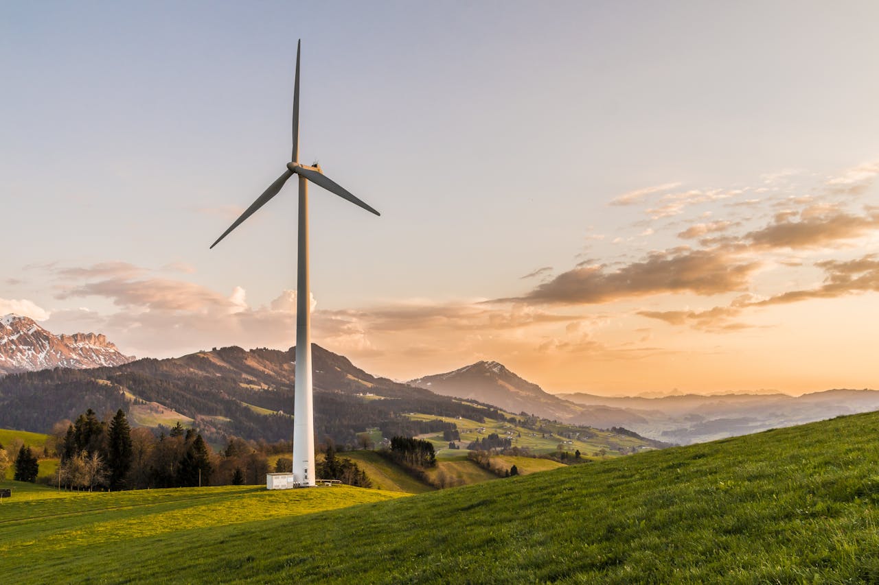 Netcongestie: knelpunten in het elektriciteitsnet Wind turbine amid rolling hills and mountains at sunset, symbolizing renewable energy and sustainability.